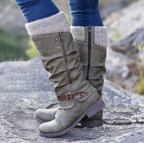 Green knee-high boots with zippers and knit cuffs worn outdoors on a rocky surface.