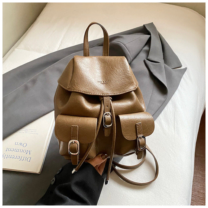 Brown leather backpack on a surface with a book and gray fabric