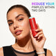 Woman holding a red skincare product with text claiming to reduce pimples within two days on a light background.