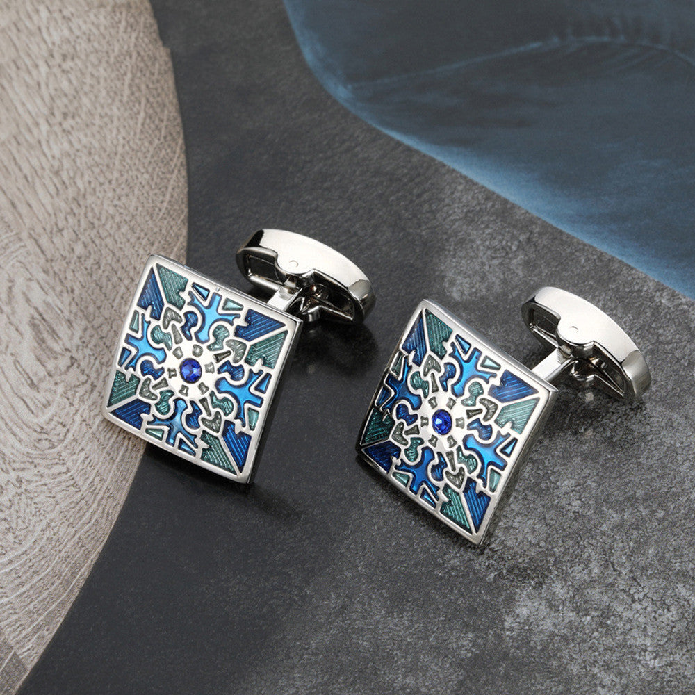 Pair of square cufflinks with blue and green pattern on a dark surface