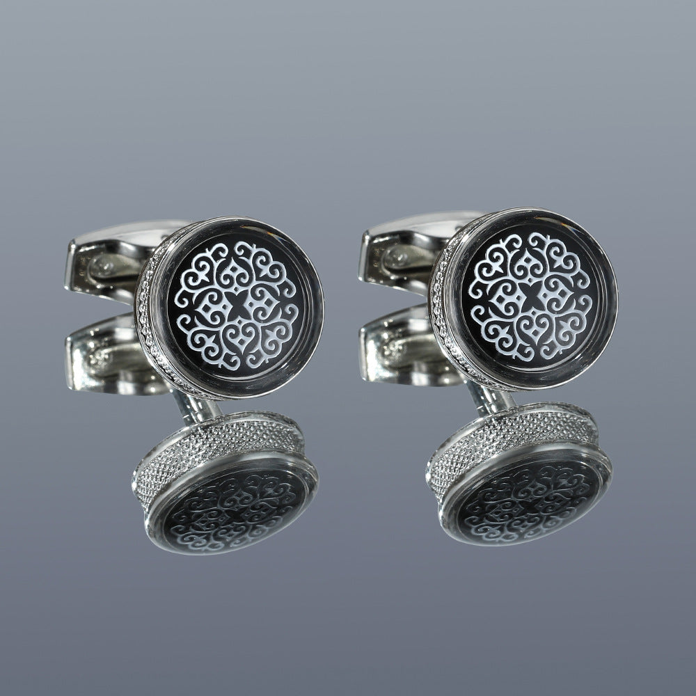 Pair of silver cufflinks with intricate black and white design on a gray background