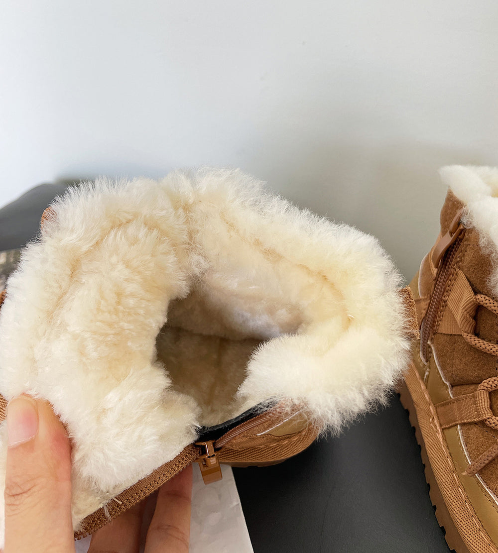 Close-up of brown winter boots with fluffy white lining held by a hand against a light background.