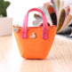 Small orange handbag with pink handles on a wooden surface