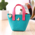 Small turquoise handbag with pink handles on a light wooden surface