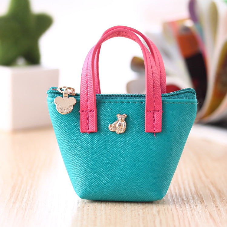 Small turquoise handbag with pink handles on a light wooden surface