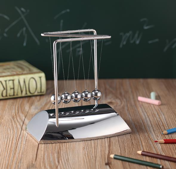 Newton's cradle on a wooden desk with books and pencils in the background