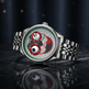 Une montre-bracelet en acier inoxydable argenté avec un cadran squelette unique présentant un crâne stylisé, des sous-cadrans circulaires rouges et un anneau intérieur vert, reposant sur une surface sombre et réfléchissante.