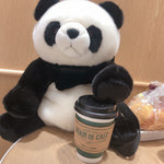 Plush panda toy holding a coffee cup on a wooden surface