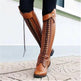 Brown knee-high boots with detailed laces worn by a person on a stone pavement.