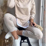 Person wearing a beige sweatshirt and pants sitting on a stool indoors.
