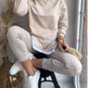 Person wearing a beige sweatshirt and pants sitting on a stool indoors.