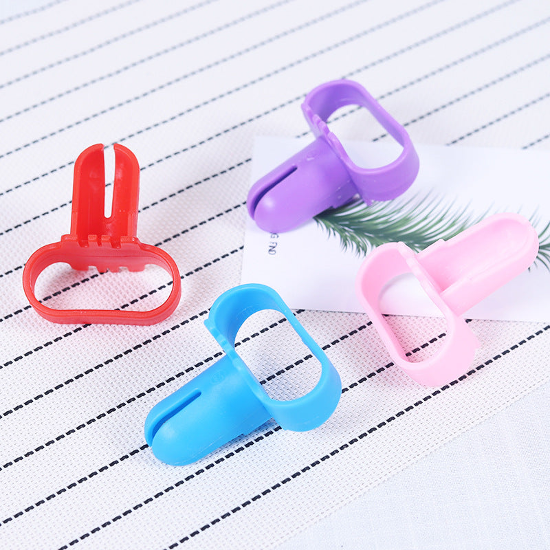 Four plastic clip-style accessories in red, purple, blue, and pink, arranged on a white textured surface with thin gray stripes and a small printed card.
