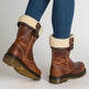 Brown ankle boots with white fur lining worn with blue jeans on a light gray background