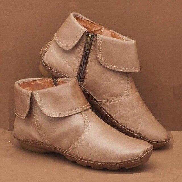 Pair of beige ankle boots with zippers on a brown background