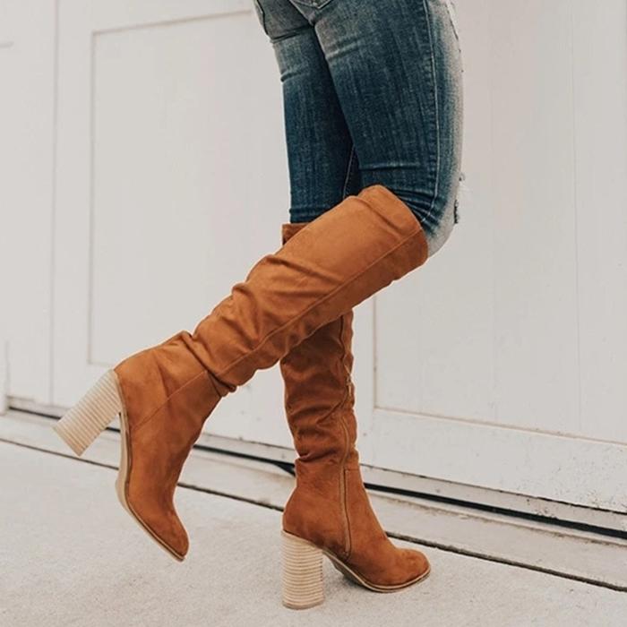 Brown knee-high boots worn with blue jeans against a white background