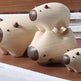 Three small wooden animal figurines with smooth natural wood bodies and dark brown snouts and ears, arranged on a wooden surface with stacked books in the background.