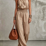 Woman wearing a beige jumpsuit holding a brown handbag against a neutral background