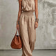Woman wearing a beige jumpsuit holding a brown handbag against a neutral background