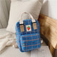 Blue plaid backpack with a strawberry patch logo on a bed