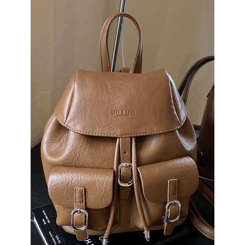 Brown leather backpack with silver buckles on a dark surface