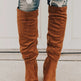 Brown knee-high boots worn with ripped jeans on a neutral background
