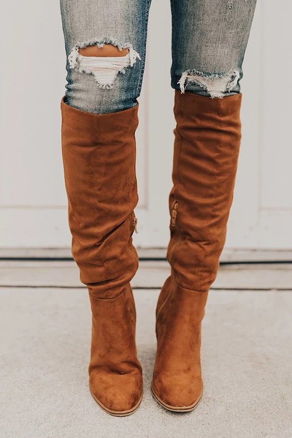 Brown knee-high boots worn with ripped jeans on a neutral background