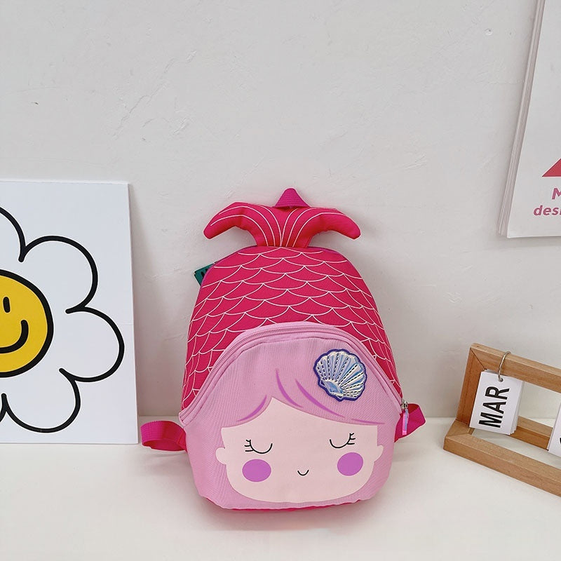 Pink mermaid-shaped children's backpack on a white surface with a white wall background