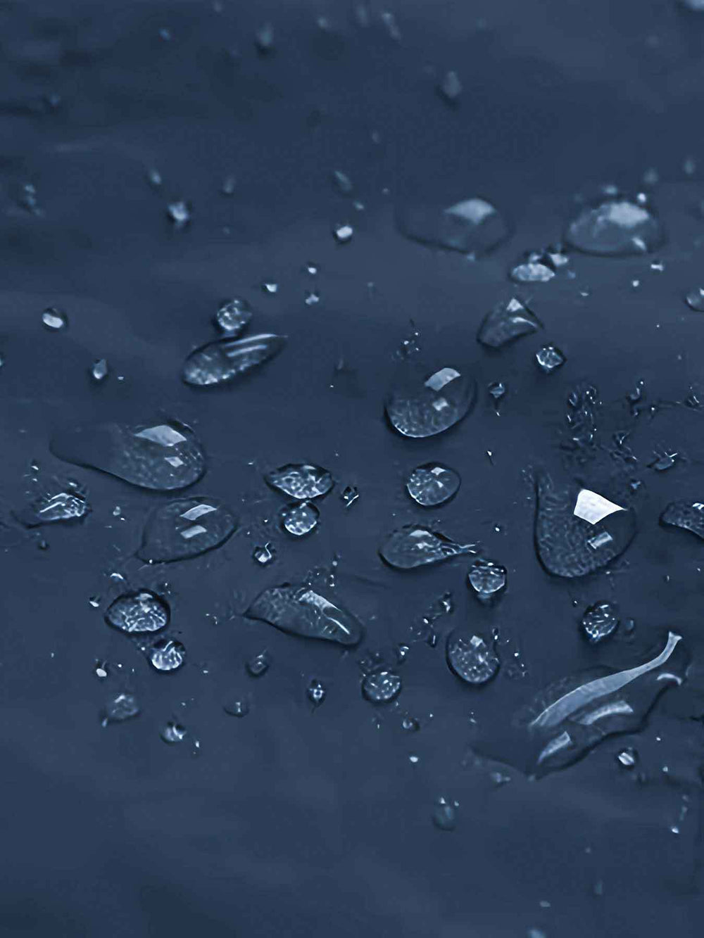 Close-up of clear water droplets resting on a dark navy blue textured surface.