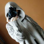 Person wearing a gray hoodie holding a camera against a brown background
