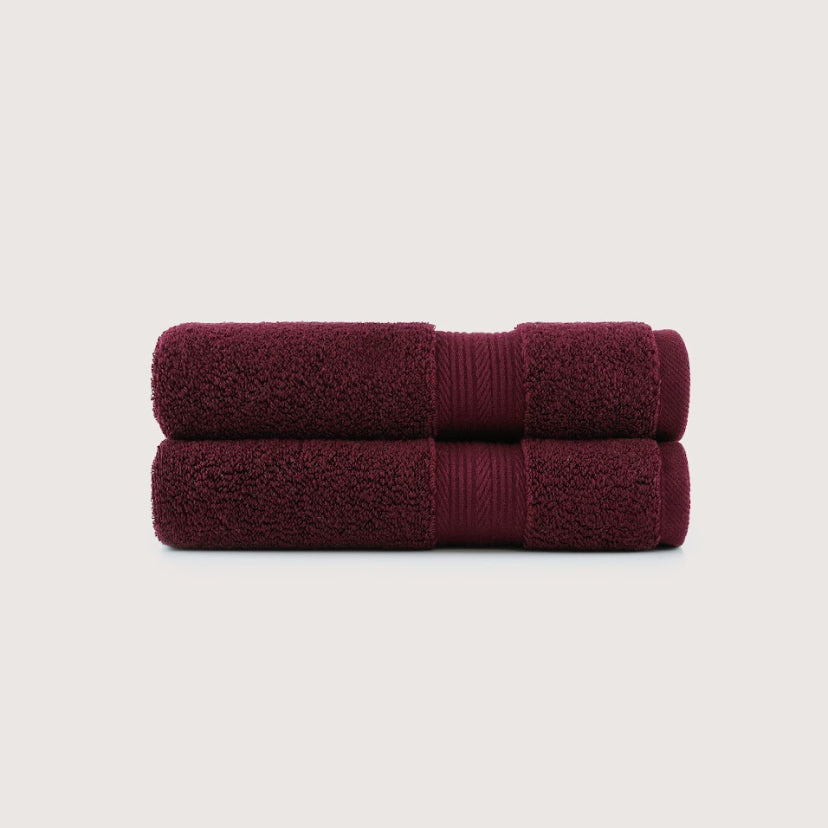 Two folded bath towels in a deep burgundy color, stacked vertically on a light beige background.