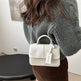 Person wearing a gray sweater holding a white handbag with a visible brand tag.