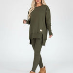 Woman wearing an olive green outfit with a sweater and leggings, standing in a modern interior setting.