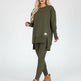 Woman wearing an olive green outfit with a sweater and leggings, standing in a modern interior setting.