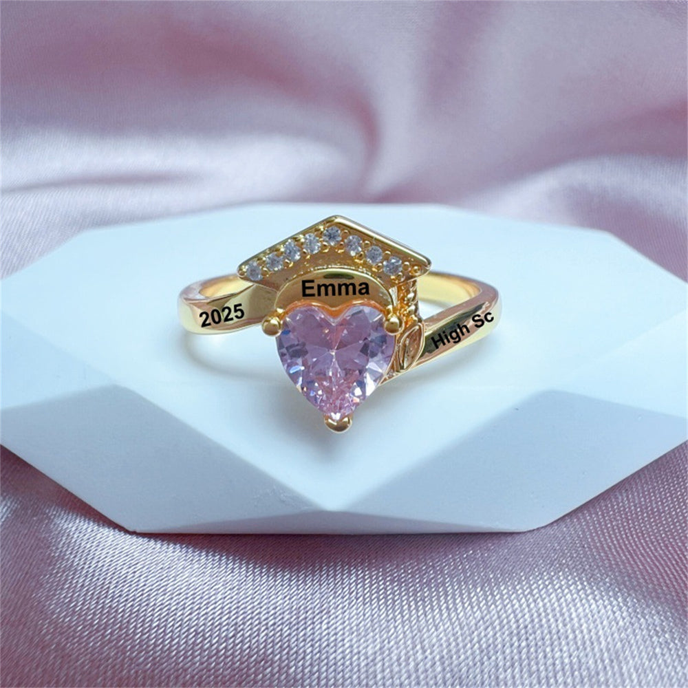 Gold ring with a heart-shaped pink gemstone on a white stand with a pink fabric background