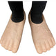 A pair of beige, foot-shaped silicone or rubber shoe covers with textured creases, shown on a person's feet wearing black socks against a white background.