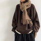 Person wearing a brown sweater and scarf with a beige bag against a white background