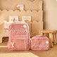 A pink corduroy backpack and matching zip pouch set with the name 'Amelia' embroidered on the front, styled on a beige rug in front of a wooden bookshelf.