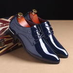 Pair of navy blue patent leather shoes with gold laces on a beige surface.