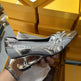 Silver high-heeled shoe held by a hand with yellow boxes in the background