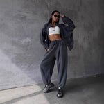 Person wearing a gray tracksuit and white crop top against a concrete wall.