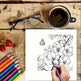Coloring book with floral design, colored pencils, a cup of coffee, and glasses on a wooden surface.