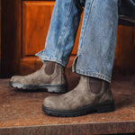 Brown leather boots worn with blue jeans on a wooden floor.