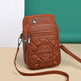 Brown leather crossbody bag with heart patterns on a beige surface and teal background