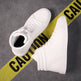 White high-top sneakers on a gray surface with yellow caution tape.