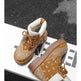 A pair of brown lace-up ankle boots with a tan bandana print overlay and white lining, displayed on a white geometric platform against a dark textured background.