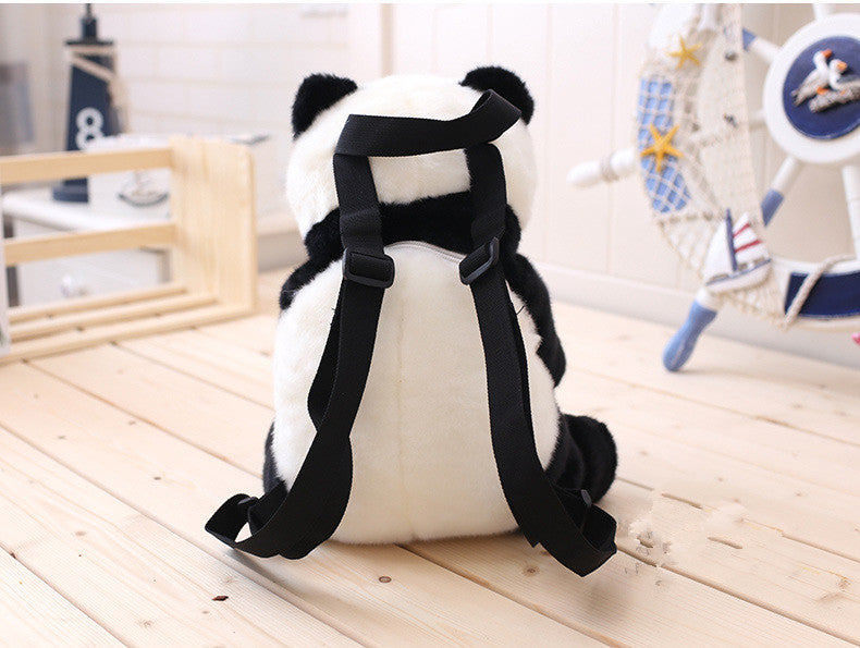 Panda-shaped plush toy with black straps on a wooden surface