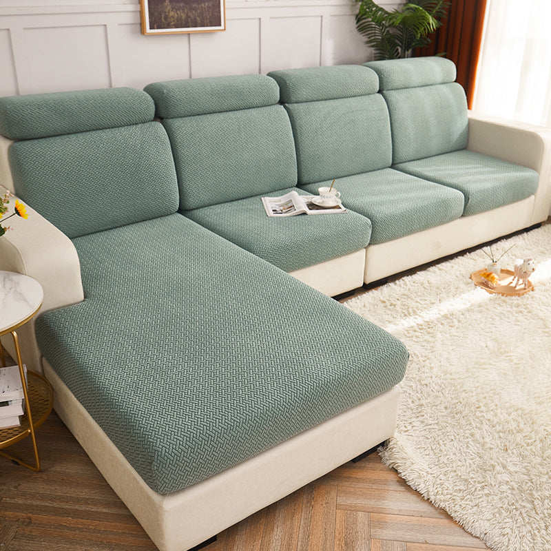 A light sage green textured sofa slipcover fitted on a sectional sofa with cream-colored arms and base, shown in a bright living room setting.