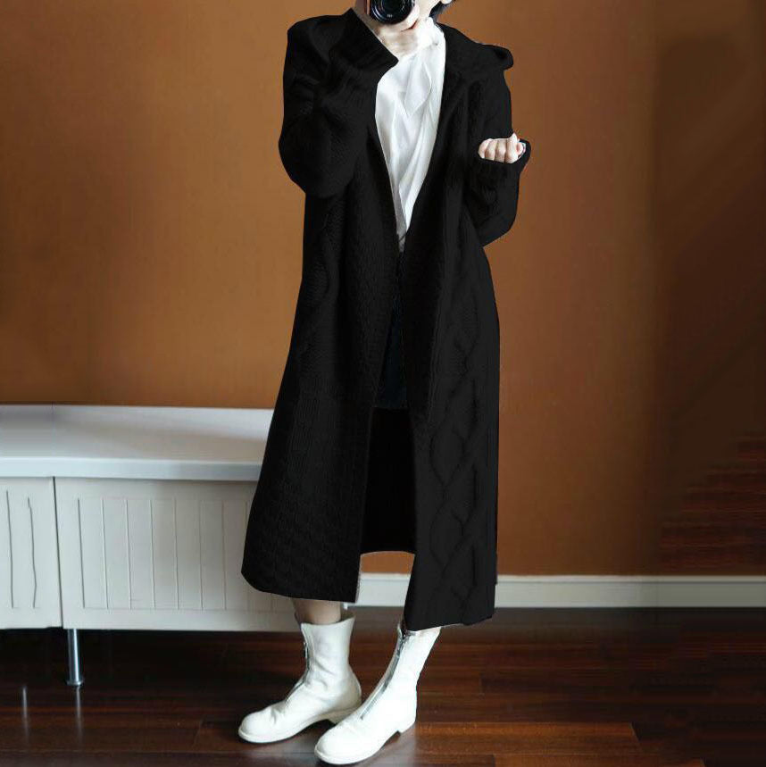 Person wearing a long black coat with a plain background