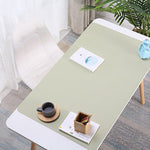 Light green desk pad on a wooden desk with a cup, saucer, and small plant in a room.