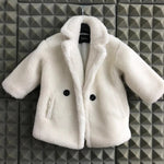 White fluffy coat with black buttons on a hanger against a geometric patterned wall.